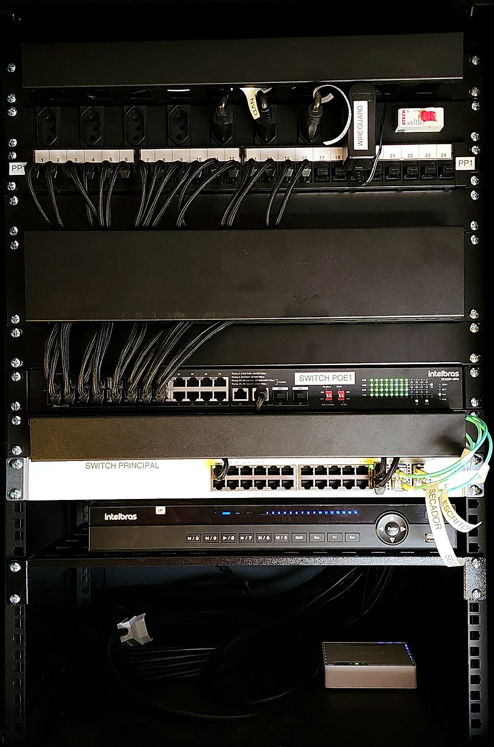 Rack de telecomunicações montado pela Guto Gheno Tecnologia: patch panel, organizadores, switch PoE, switch principal, NVR e roteador
